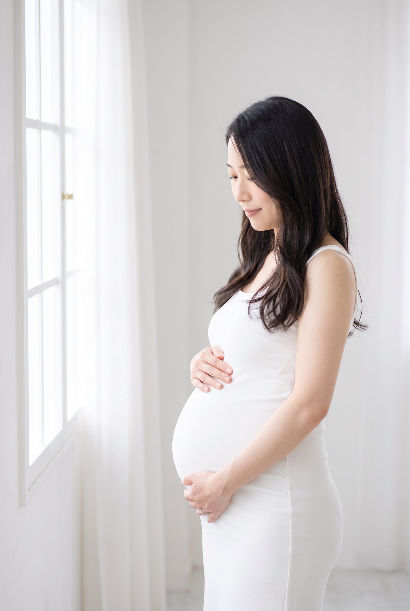 明るい窓辺で、お腹に手を添える妊婦